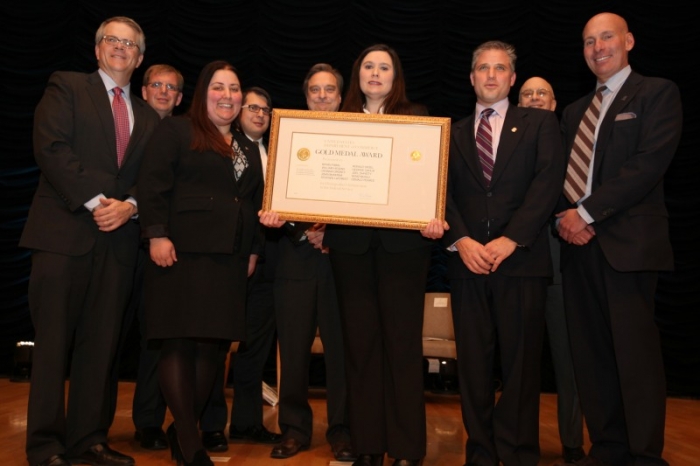 The ITA team holding their Gold Medal Award aside Deputy Secretary Andrews.