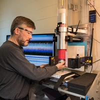 NIST Materials Scientist Michael Riley prepares a sample of material for a drop test that will reveal its ability to absorb and dissipate energy. This was one of a series of tests that helped the Head Health III judges identify five materials that held th